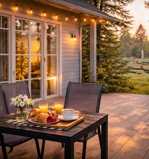 A wooden deck with a table set for breakfast, including croissants, fruit, and coffee. - Holiday Home in a Holiday Park Rewal at 600 m From the sea (Rewal)