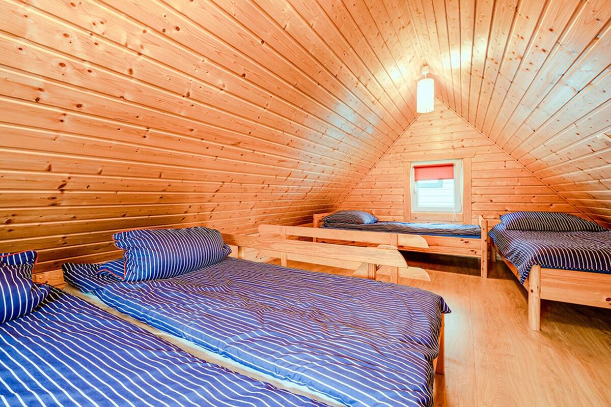 A cozy cabin with three wooden beds, a small window, and a wooden ceiling.