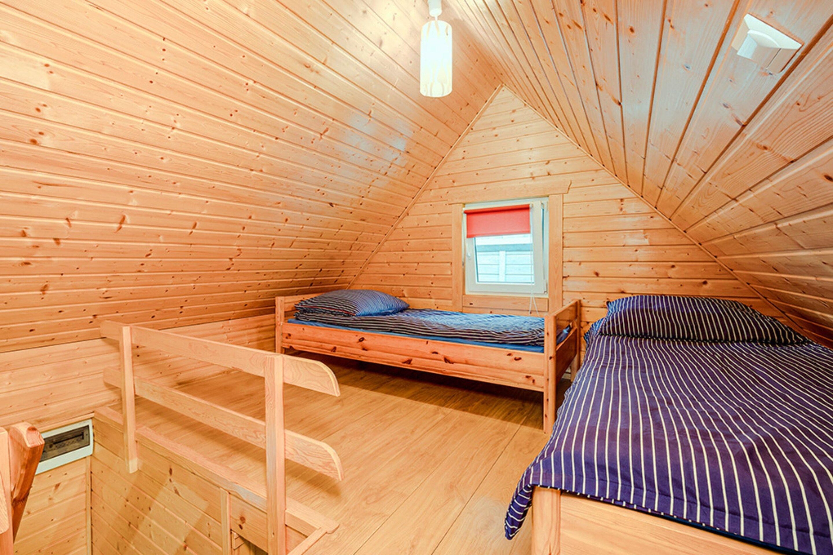 Una baita di legno con una camera da letto mansardata, una finestra con persiana rossa e una scala di legno.