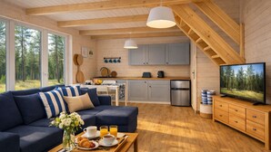 Een knus interieur van een blokhut met een bank, ontbijttafel, keuken en een televisie.
