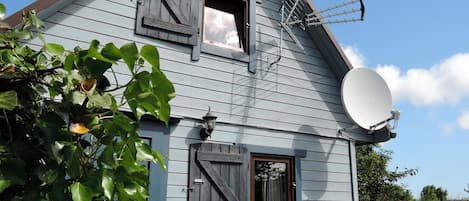 Una casa con antena parabólica, puerta de madera y ventana con contraventanas.