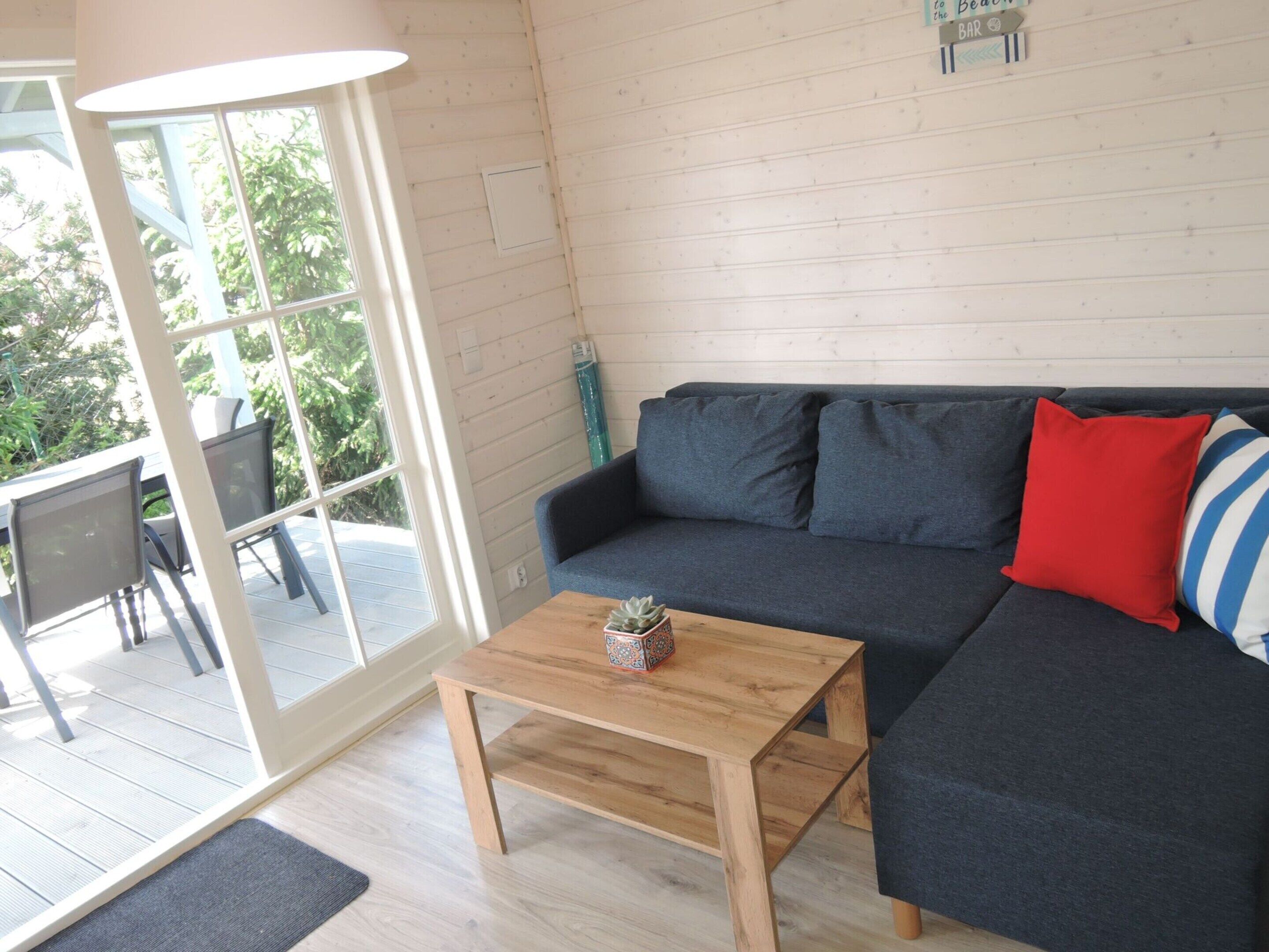 Una sala de estar moderna con un sofá gris oscuro, una mesa de centro de madera y un ventanal de vidrio que da a un patio exterior.