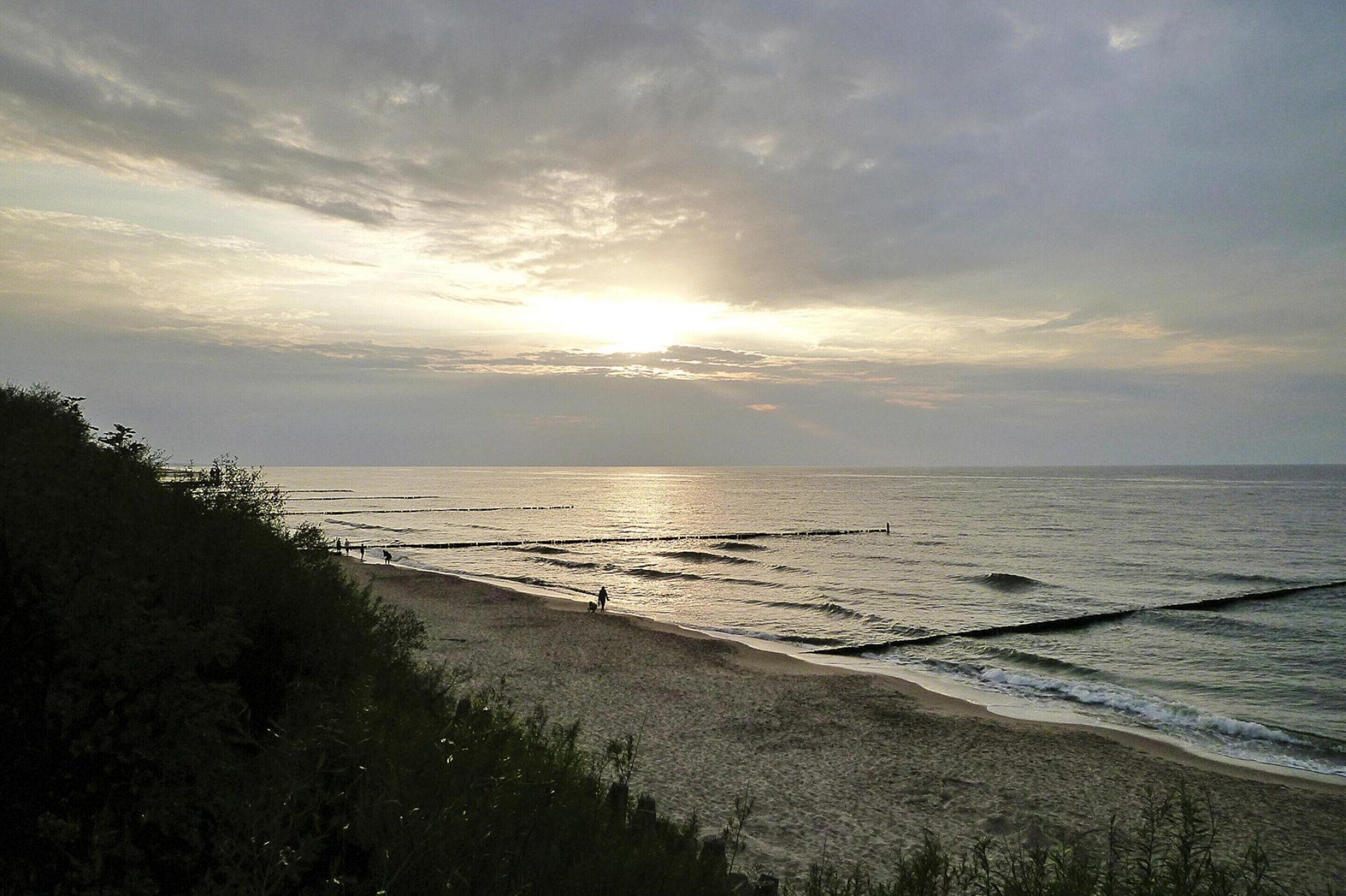 Ein Strand mit Wellen und einem Sonnenuntergang im Hintergrund.