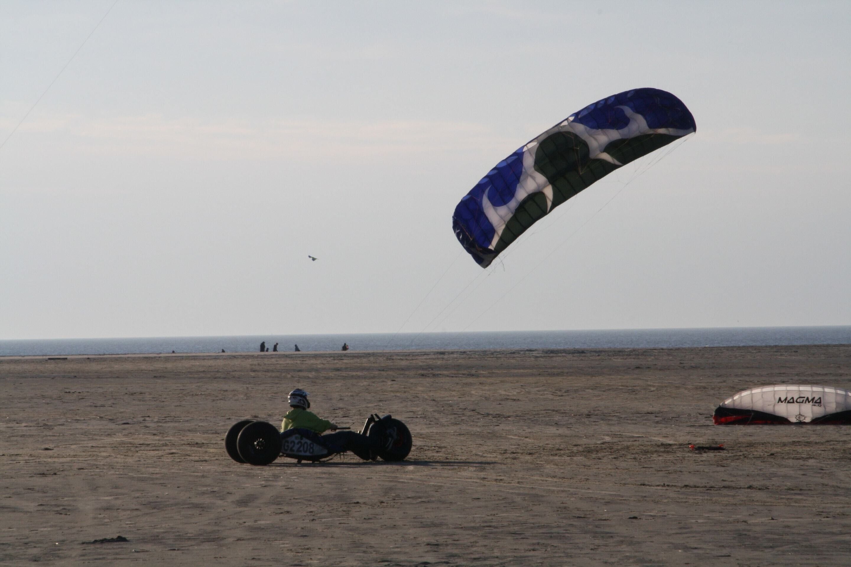 A person on a dune buggy with a parachute on the beach.