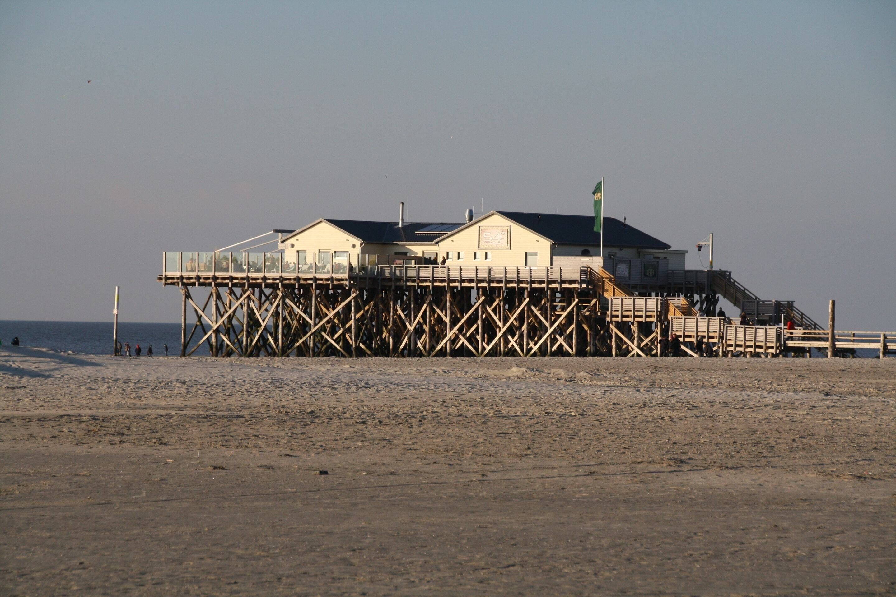 A beach house with a wooden deck and a staircase leading to the main building.