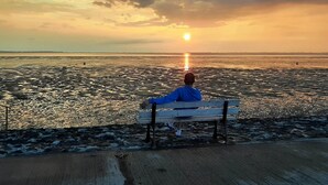 Uma pessoa sentada num banco admirando o pôr do sol sobre a água.