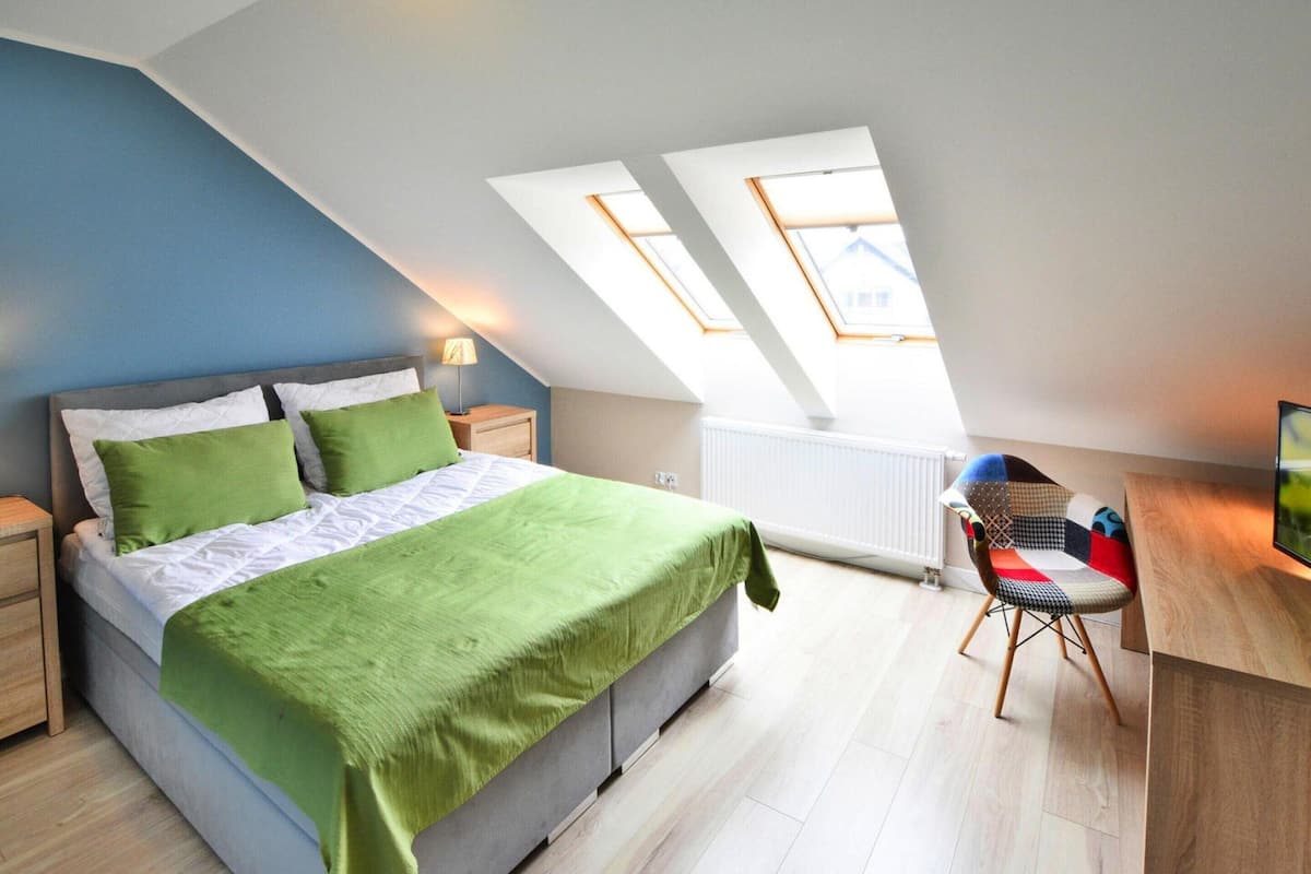 Un dormitorio con cama, almohadas verdes, escritorio y silla.