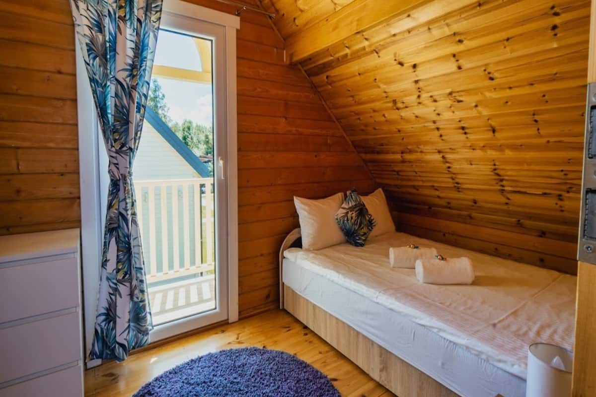 Acogedora habitación de cabaña de madera con cama, ventana con cortinas y vistas a una terraza.