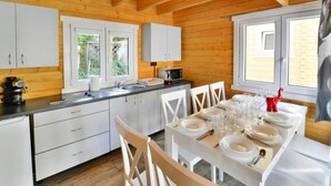 Eine Holzhütte mit einer Küche und einem Essbereich. Weiße Schränke, ein Spülbecken, eine Mikrowelle und ein für das Essen gedeckter Tisch sind vorhanden.