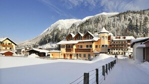 A snow-covered resort with multiple buildings, including a prominent lodge with a snow-covered roof and a mountain backdrop.