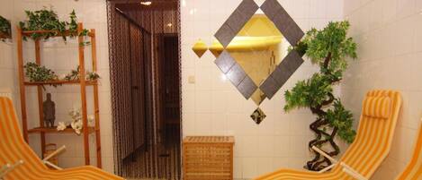 A room with two striped lounge chairs, a small wooden crate, a potted plant, and a decorative mirror on the wall.