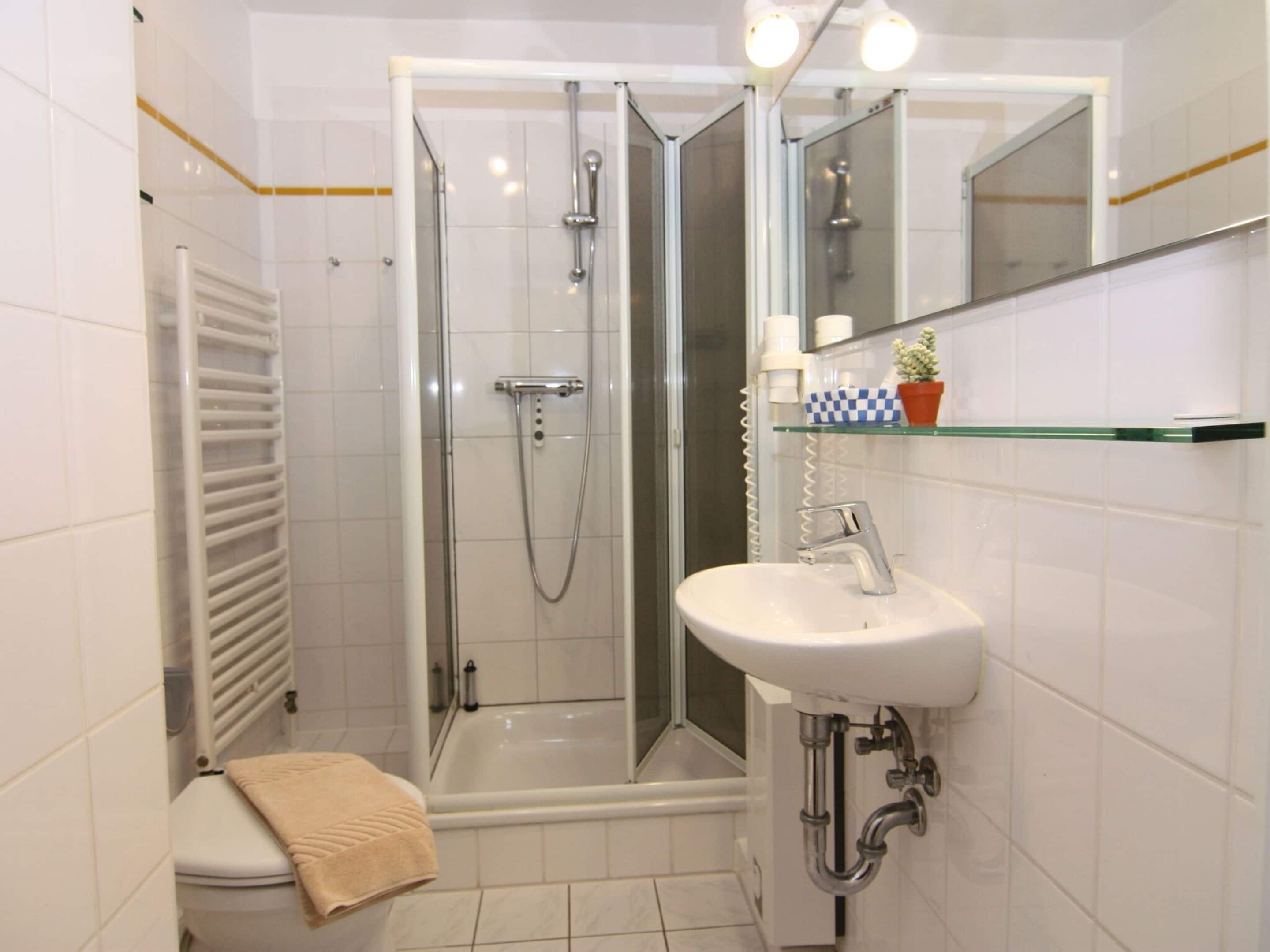 Un baño moderno con cabina de ducha de vidrio, un lavamanos blanco con grifo cromado y un estante de vidrio con artículos de aseo.
