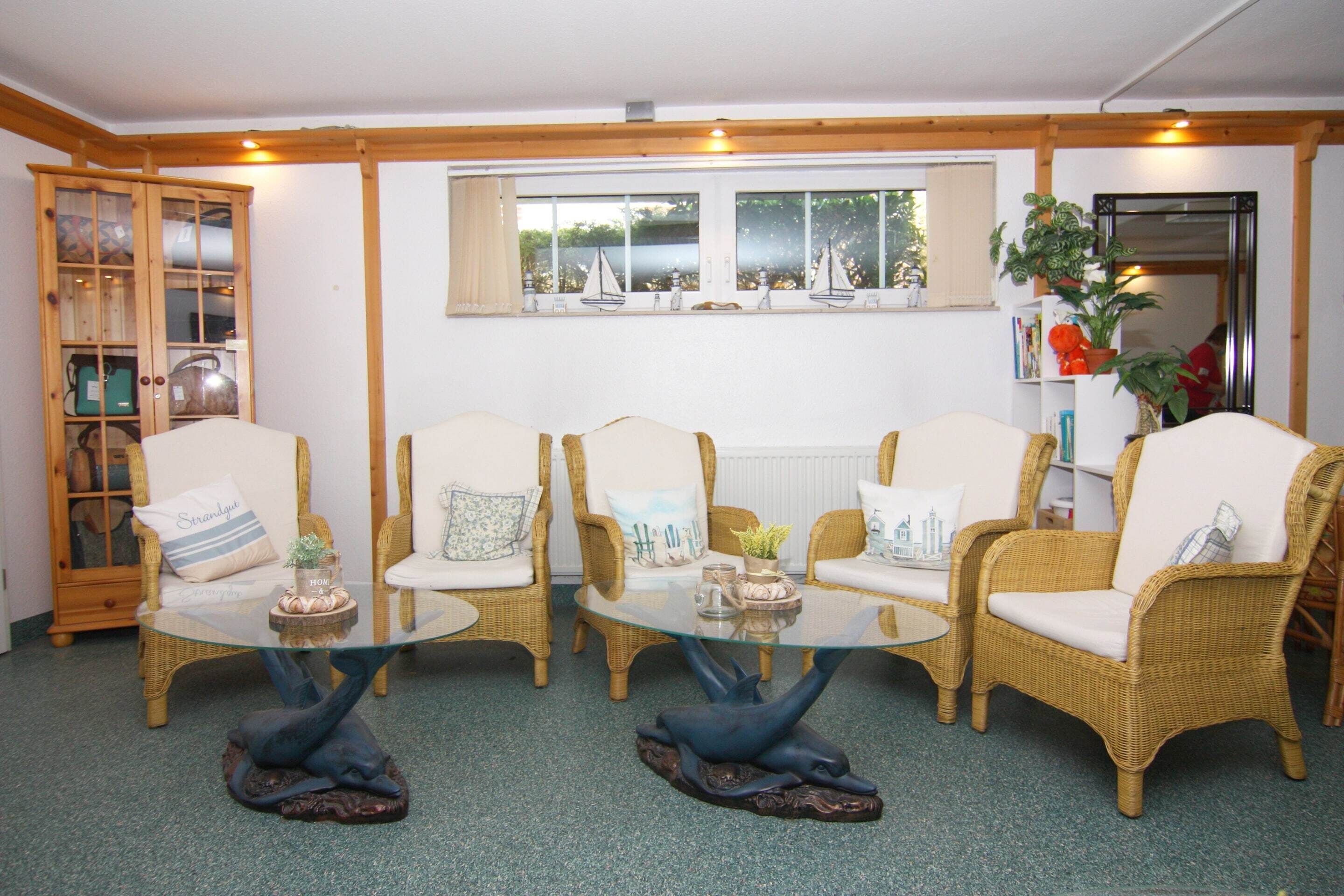A cozy room with wicker furniture, a glass coffee table, and a view of sailboats through a window.