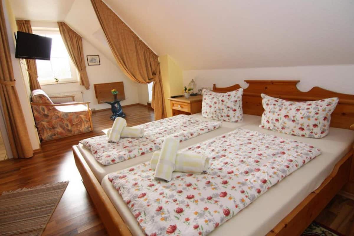 A bedroom with two single beds, a TV, a chair, and a window with curtains.