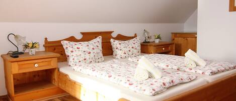 A wooden bed with floral bedding, a nightstand with a lamp, and a small table with a plant.