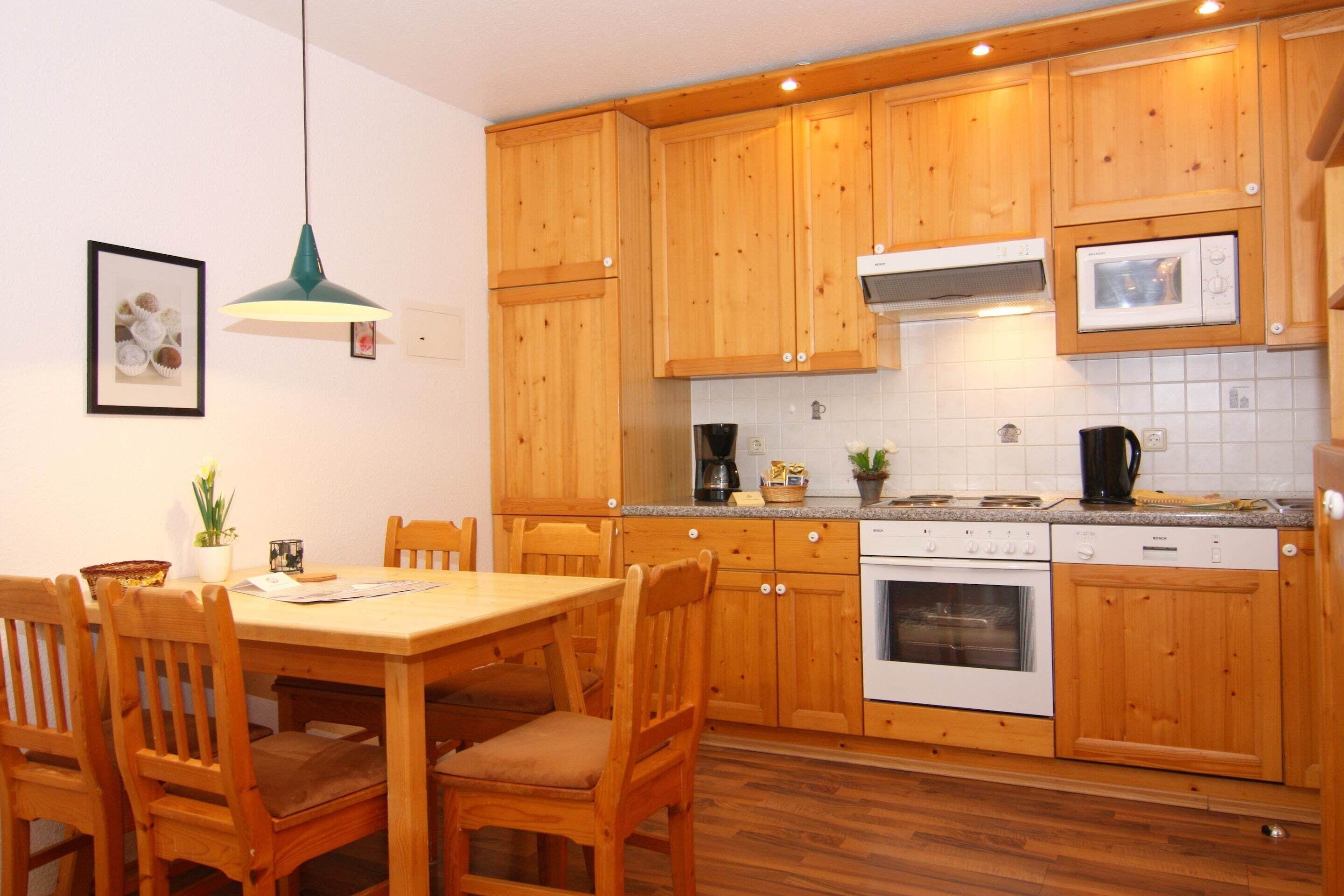 A kitchen with wooden cabinets, a dining table with chairs, a hanging light fixture, and a microwave.