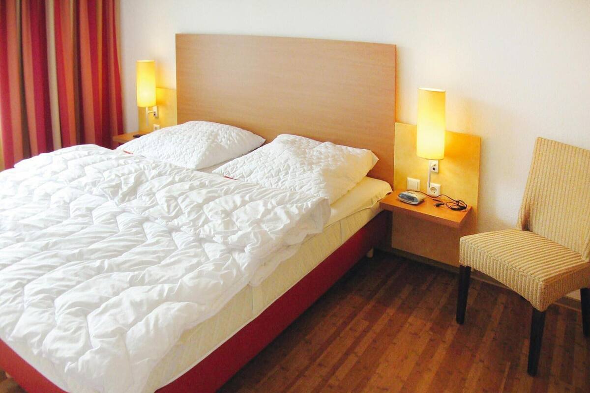 Une chambre d’hôtel avec un grand lit, deux lampes de chevet, une chaise et un plancher en bois.