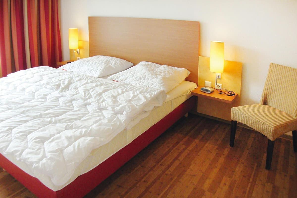 Une chambre d’hôtel avec un grand lit, deux lampes de chevet, une chaise et un plancher en bois.