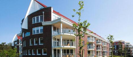 Un edificio residencial de varios pisos con balcones, fachada de ladrillo y cielo despejado.