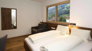 A bedroom with a wooden bed, a chair, a window with a view of a mountain, and a mirror on the wall. - Apartment in Aschau at the Lake (Aschau Im Zillertal)