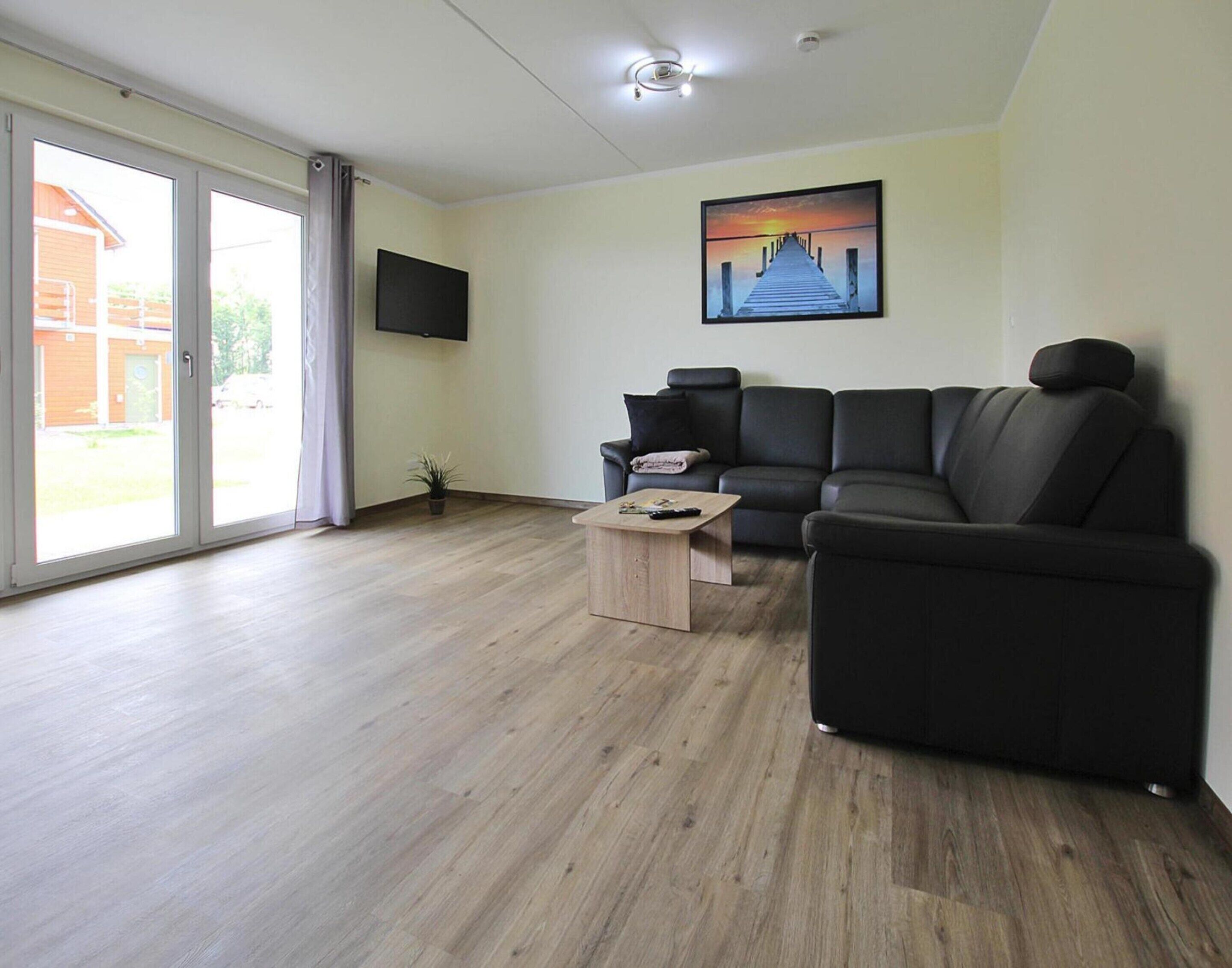 A modern living room with a black leather sofa, a wooden coffee table, and a flat-screen TV mounted on the wall.