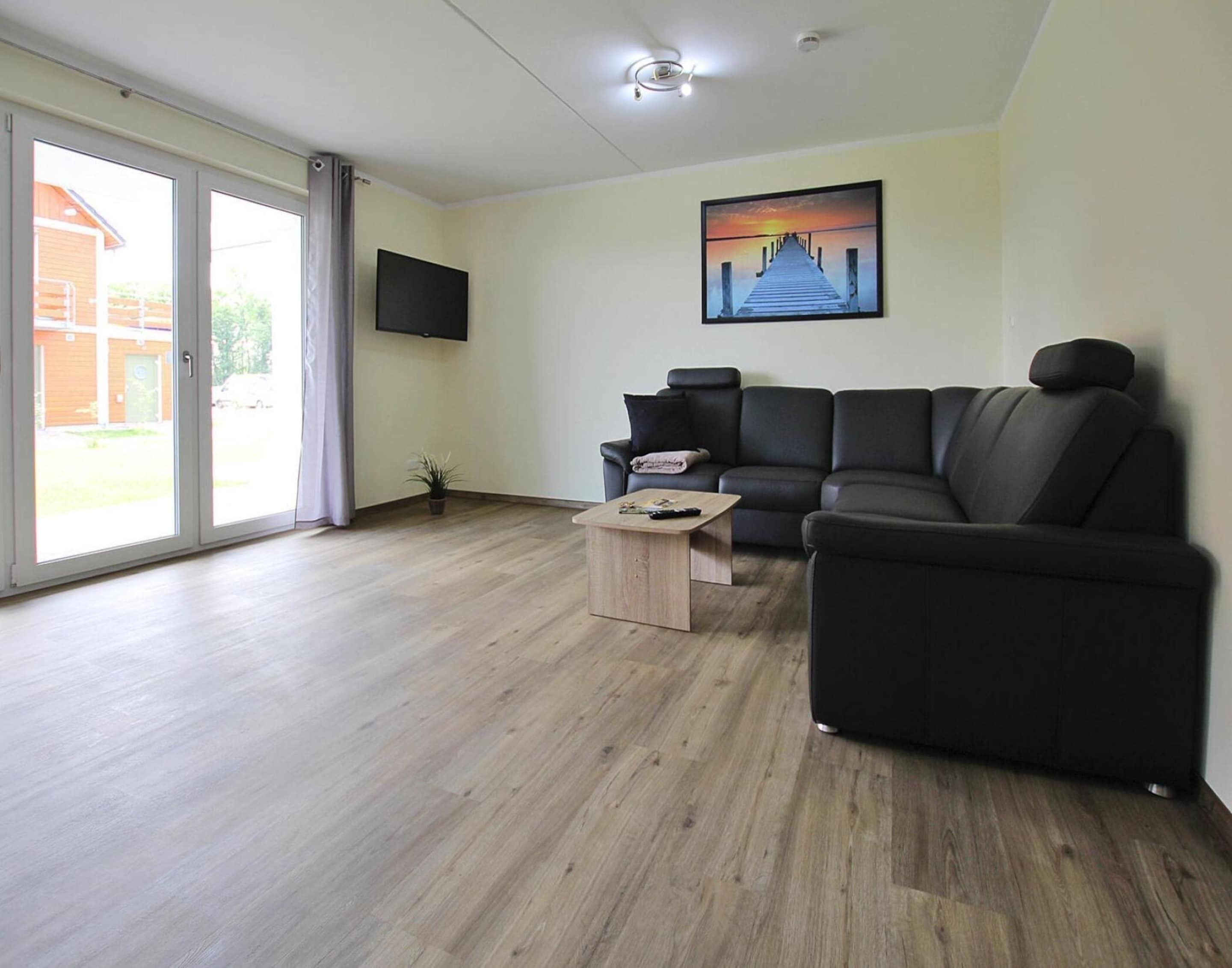 Una sala de estar moderna con un sofá de cuero negro, una mesa de centro de madera y un televisor de pantalla plana montado en la pared.