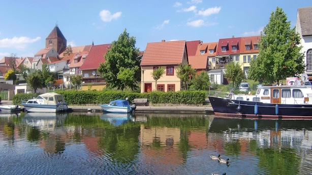 Ein ruhiger Wasserweg mit Booten, einer Ente und Gebäuden am Ufer.