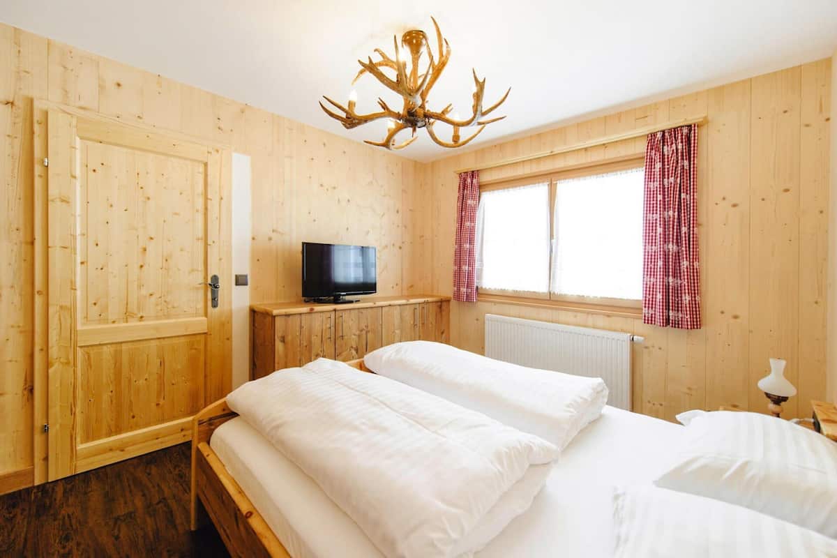 A wooden room with a bed, a television, and a window with curtains.