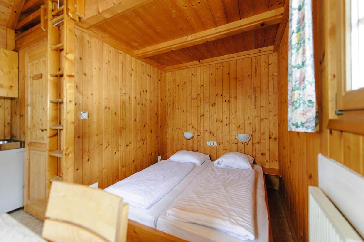 A wooden cabin room with two beds, a wooden ladder, and a small kitchenette.