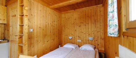 Une chambre dans un chalet en bois, avec deux lits, une échelle en bois et une petite kitchenette.
