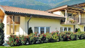 Une maison à deux étages dotée d’un balcon, entourée d’un jardin bien entretenu où poussent des fleurs rouges.