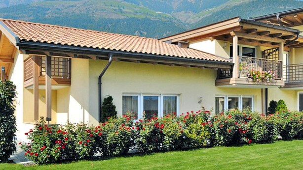 A two-story house with a balcony, surrounded by a well-maintained garden with red flowers. - Apartment in Schlanders With Terrace (Silandro)