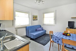 A compact kitchen with a sink, a blue sofa, a dining table with a fruit bowl, and a television. - Apartment in Schlanders With Terrace (Silandro)