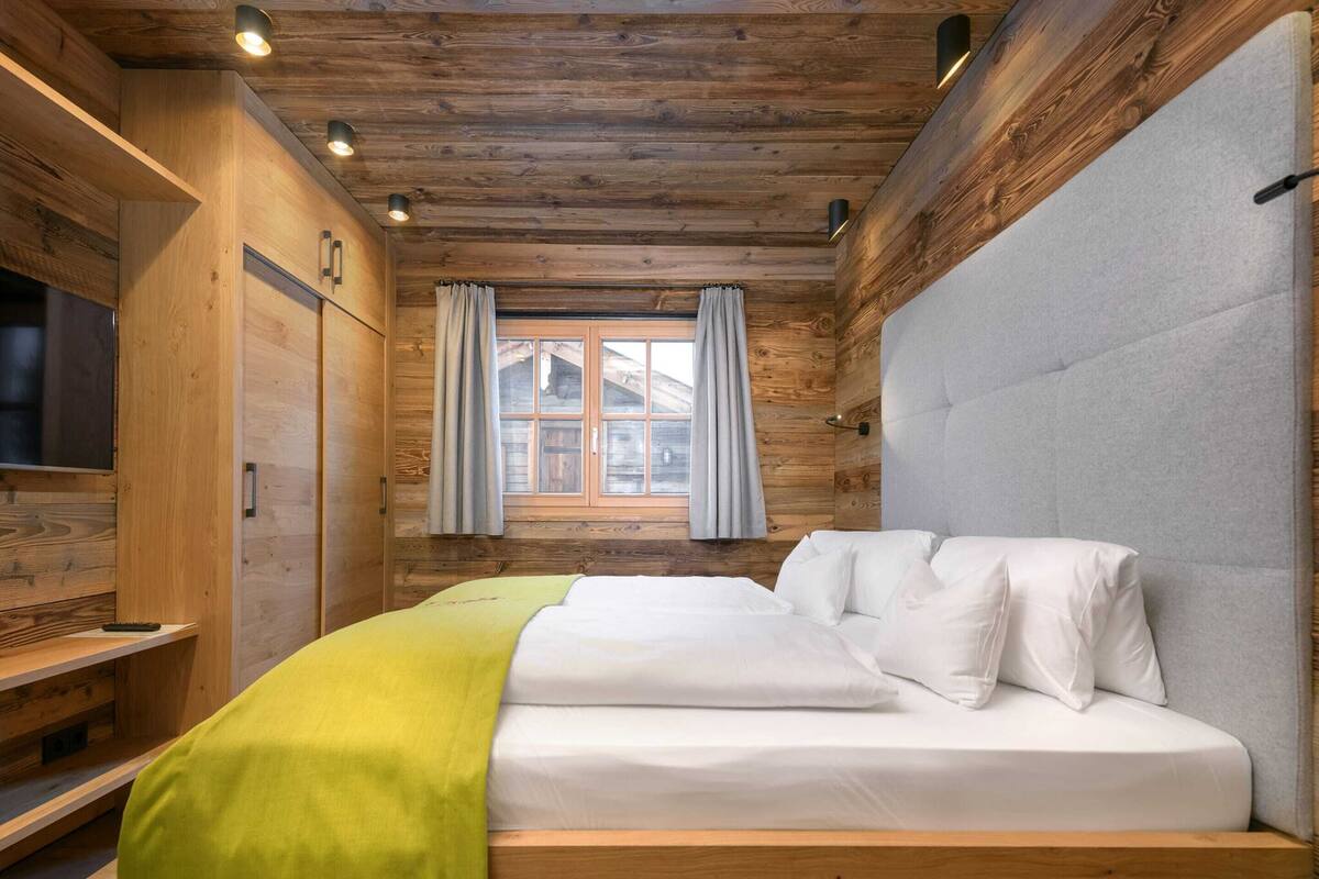 A wooden cabin room with a bed, a television, and a window with curtains.