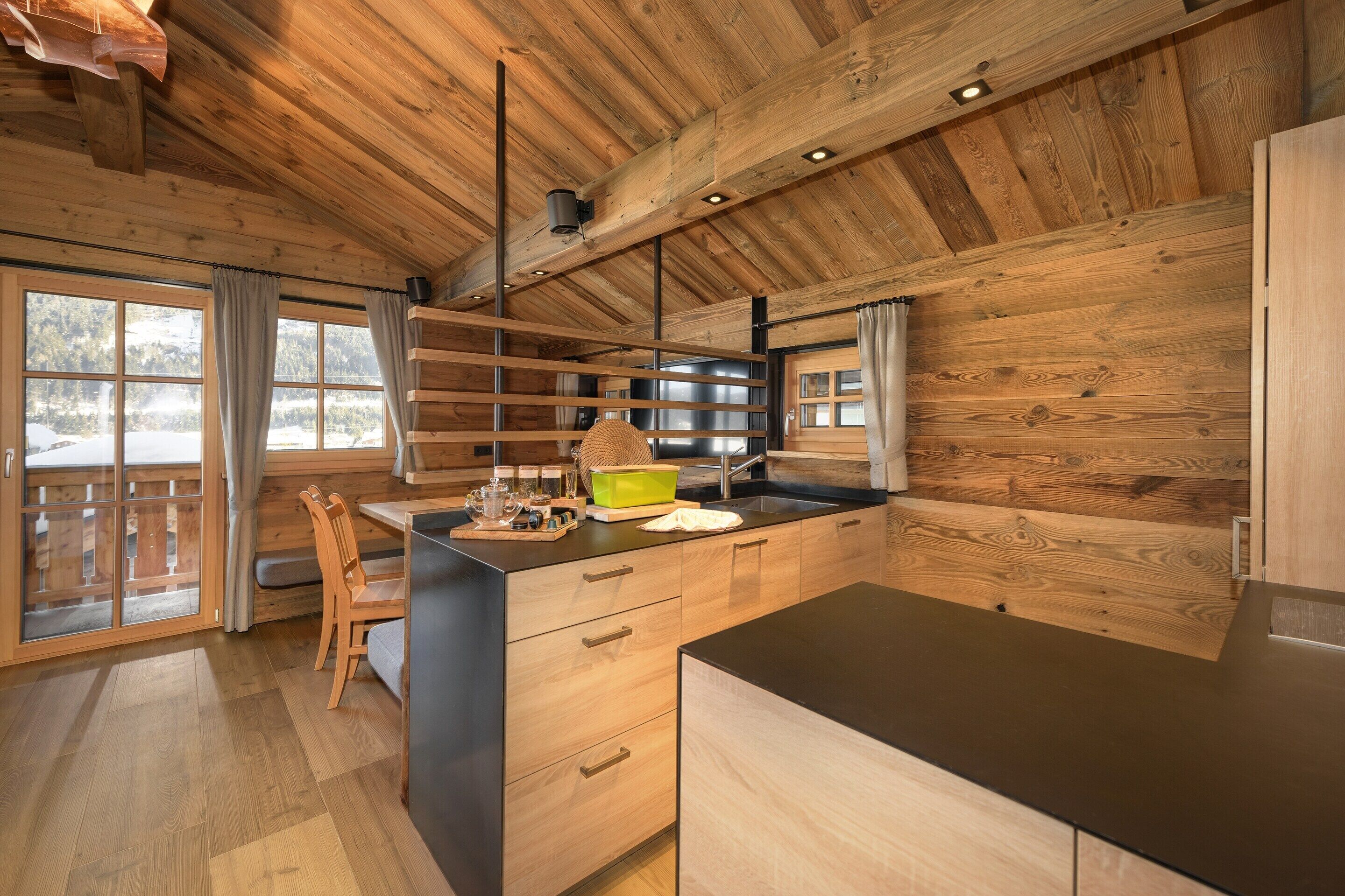 A modern kitchen with wooden cabinetry, a black countertop, and a window overlooking a snowy landscape.