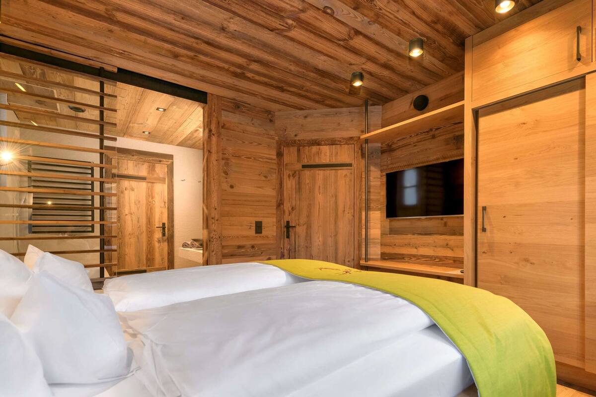 A wooden cabin-style room with two beds, a TV, and a sliding door.