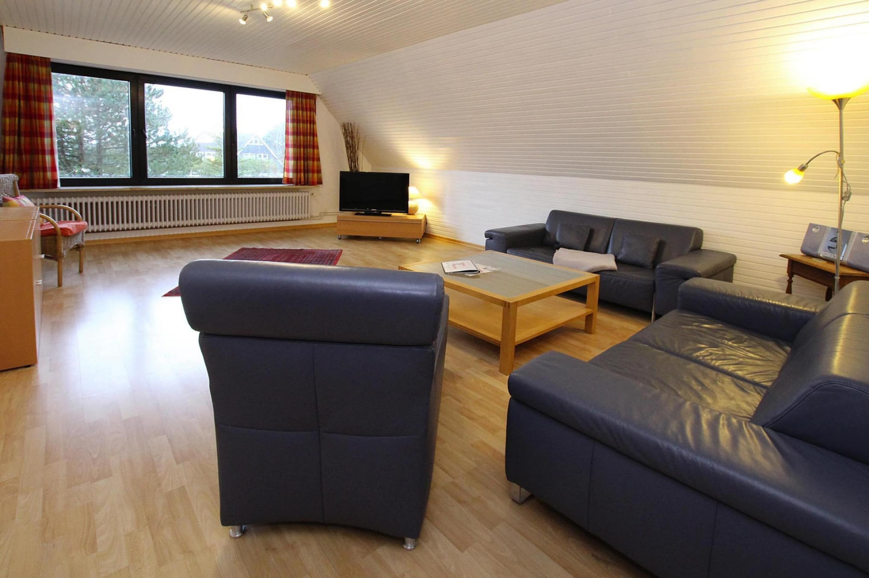 A modern living room with a large window, a flat-screen TV, and a sofa set.