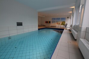An indoor swimming pool with tiled walls and a bench.