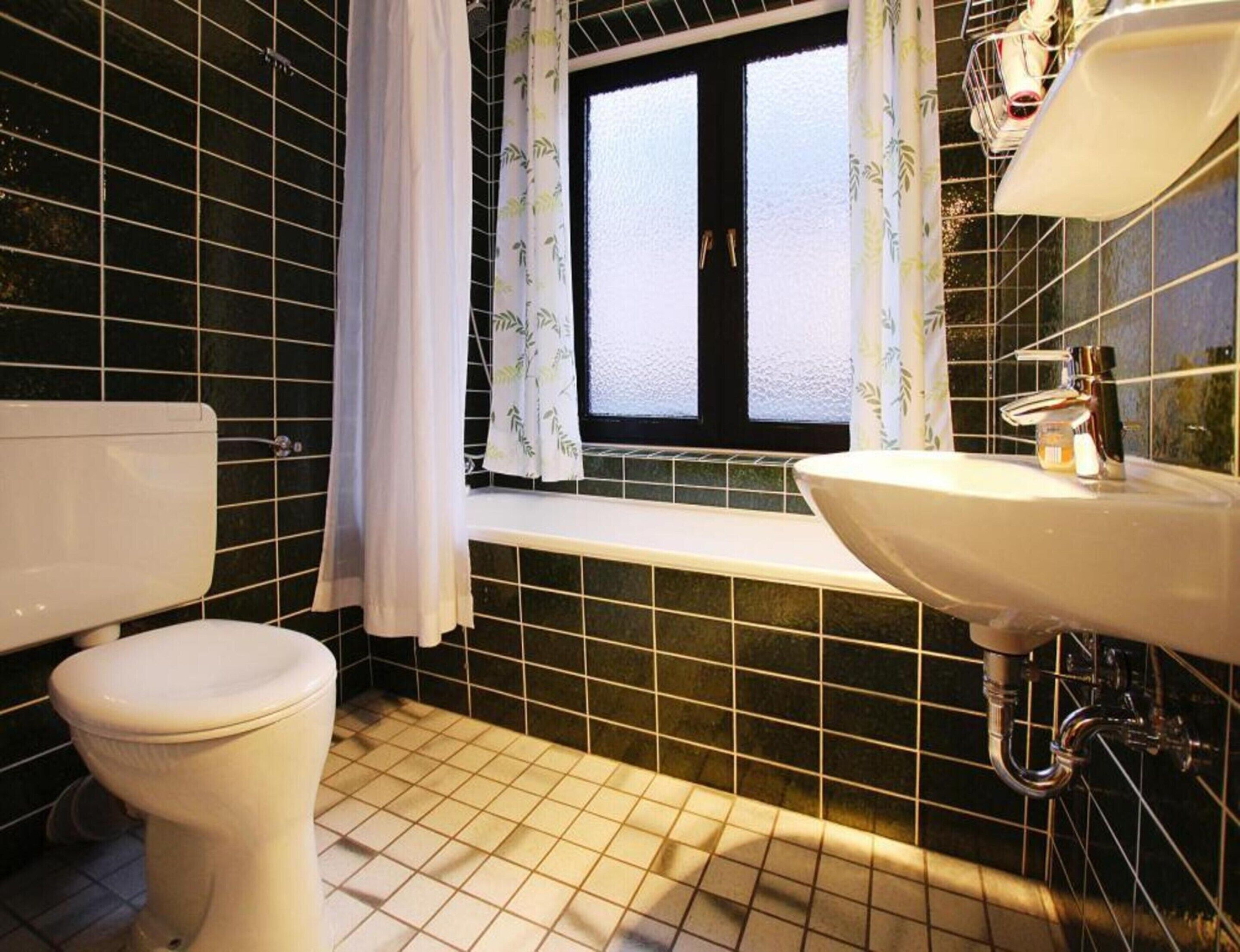 A bathroom with a toilet, a sink, and a window with curtains.