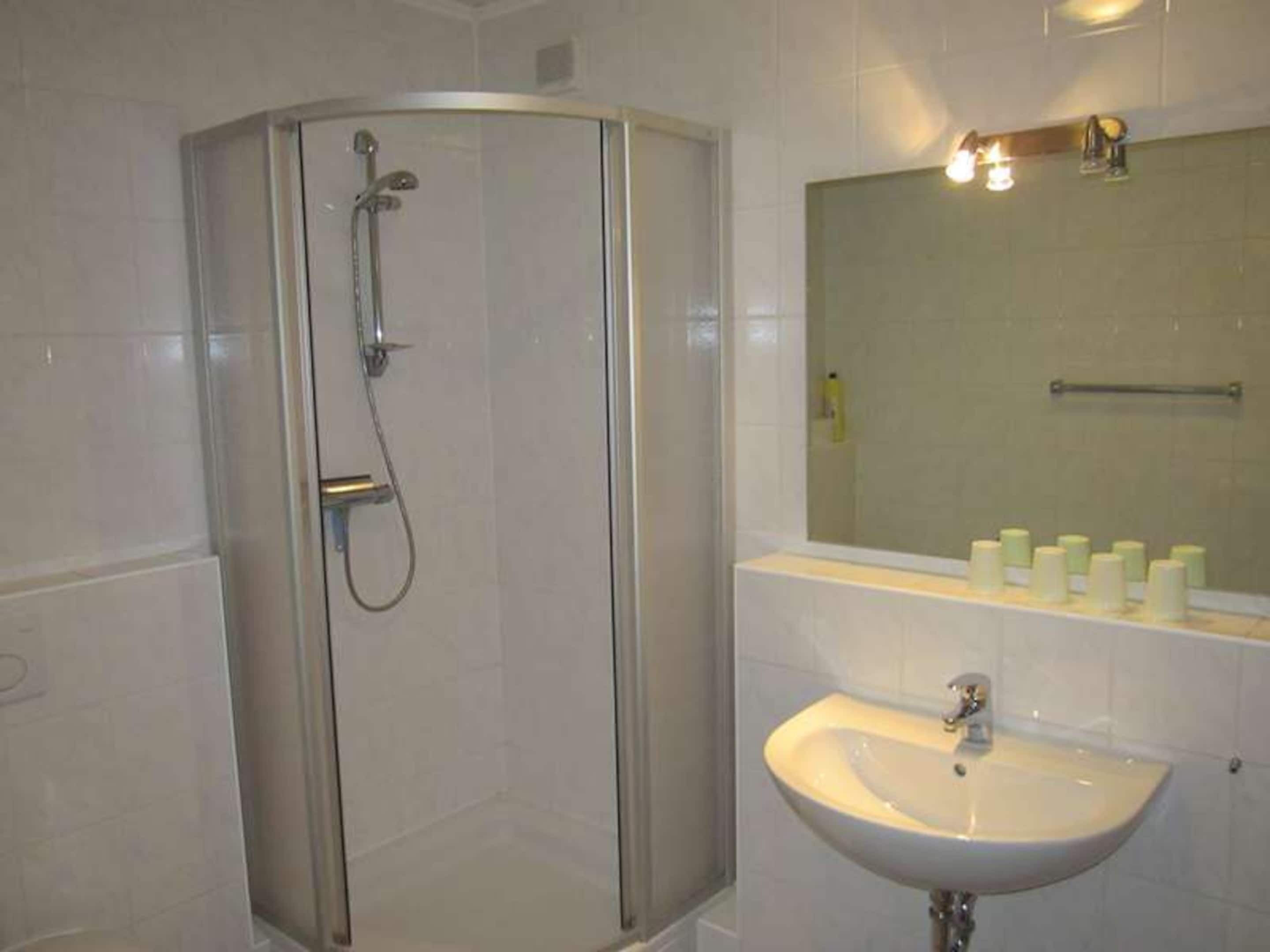 A bathroom with a glass-enclosed shower, a sink, and a mirror above it.