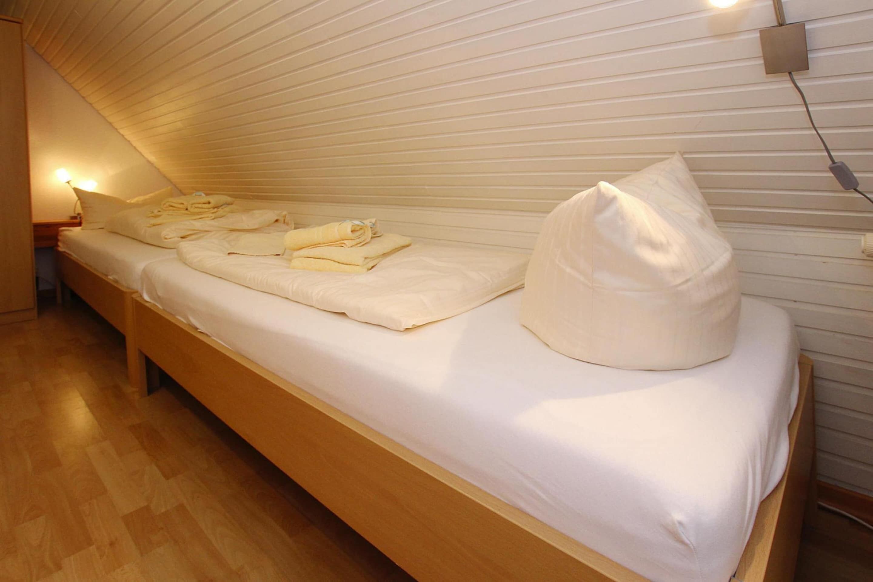 Ein Einzelbett mit ordentlich gefalteten Handtüchern und Kissen, ein Nachttisch mit Lampe sowie eine Holzbank.