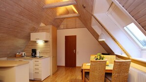 A cozy attic room with a kitchen, dining area, and a large skylight.