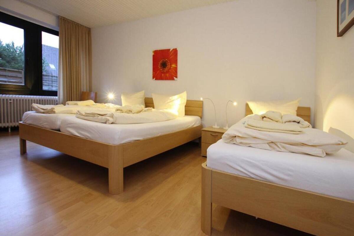 A hotel room with two wooden beds, white bedding, a radiator, and a window with curtains.