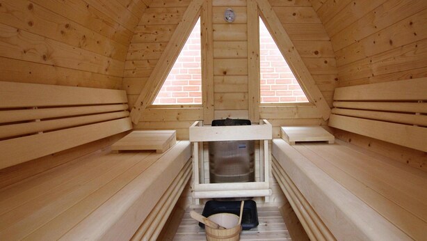 A wooden sauna with two benches, a bench heater, and a bucket.
