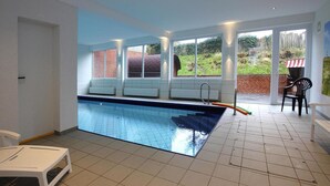 An indoor swimming pool with a view of a brick wall and greenery outside.