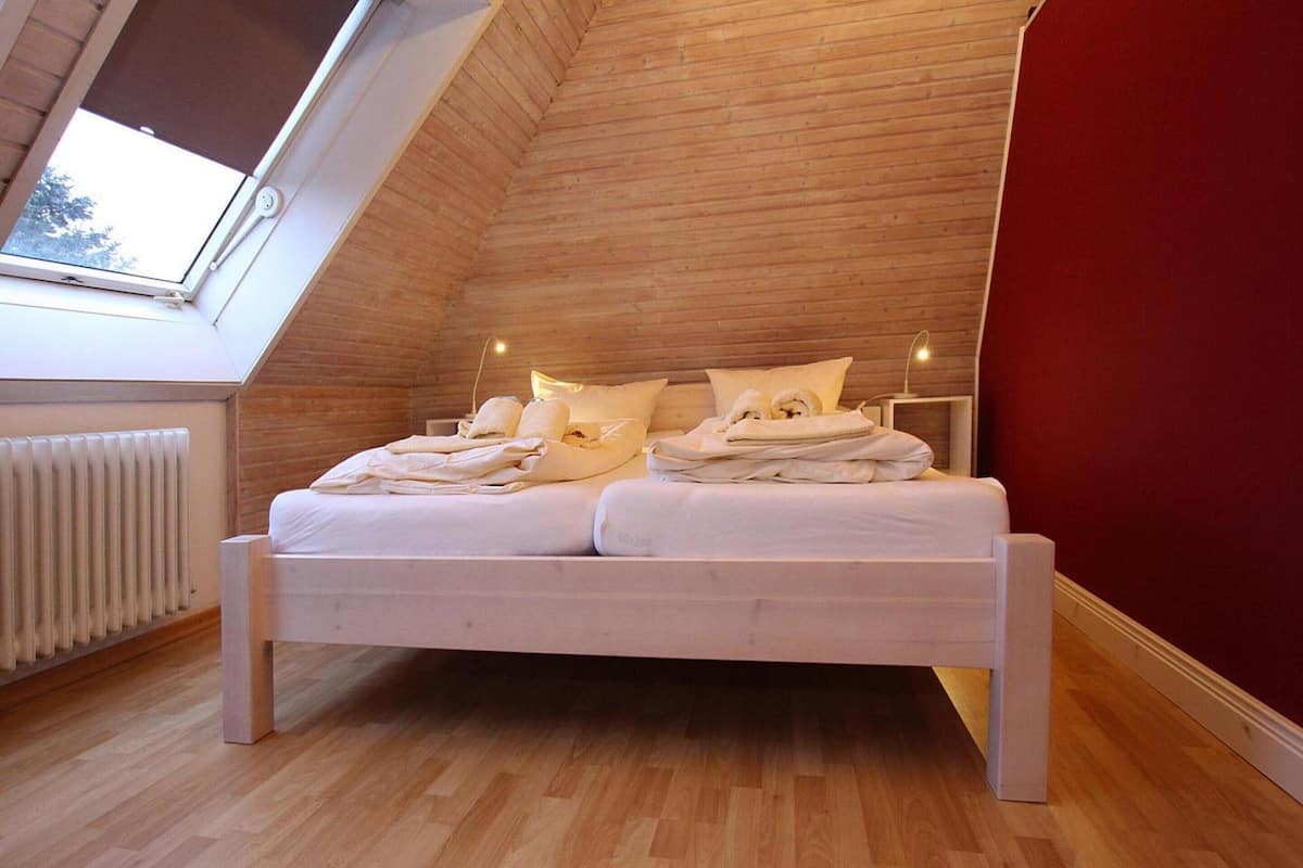 A bedroom with a sloped ceiling, a bed with white bedding, a radiator, and a window.
