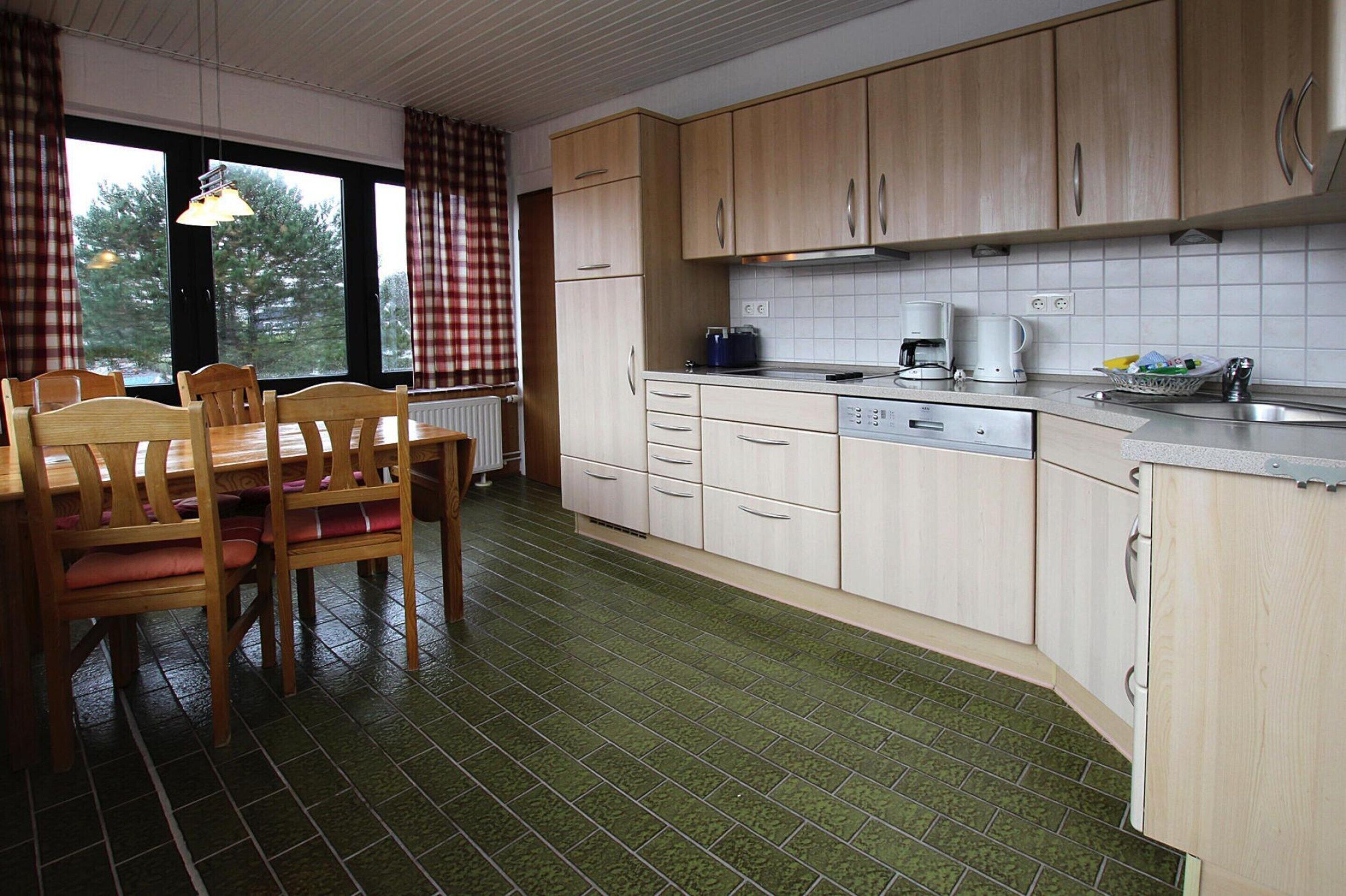 A kitchen with wooden cabinets, a dining table with chairs, and a green tiled floor.