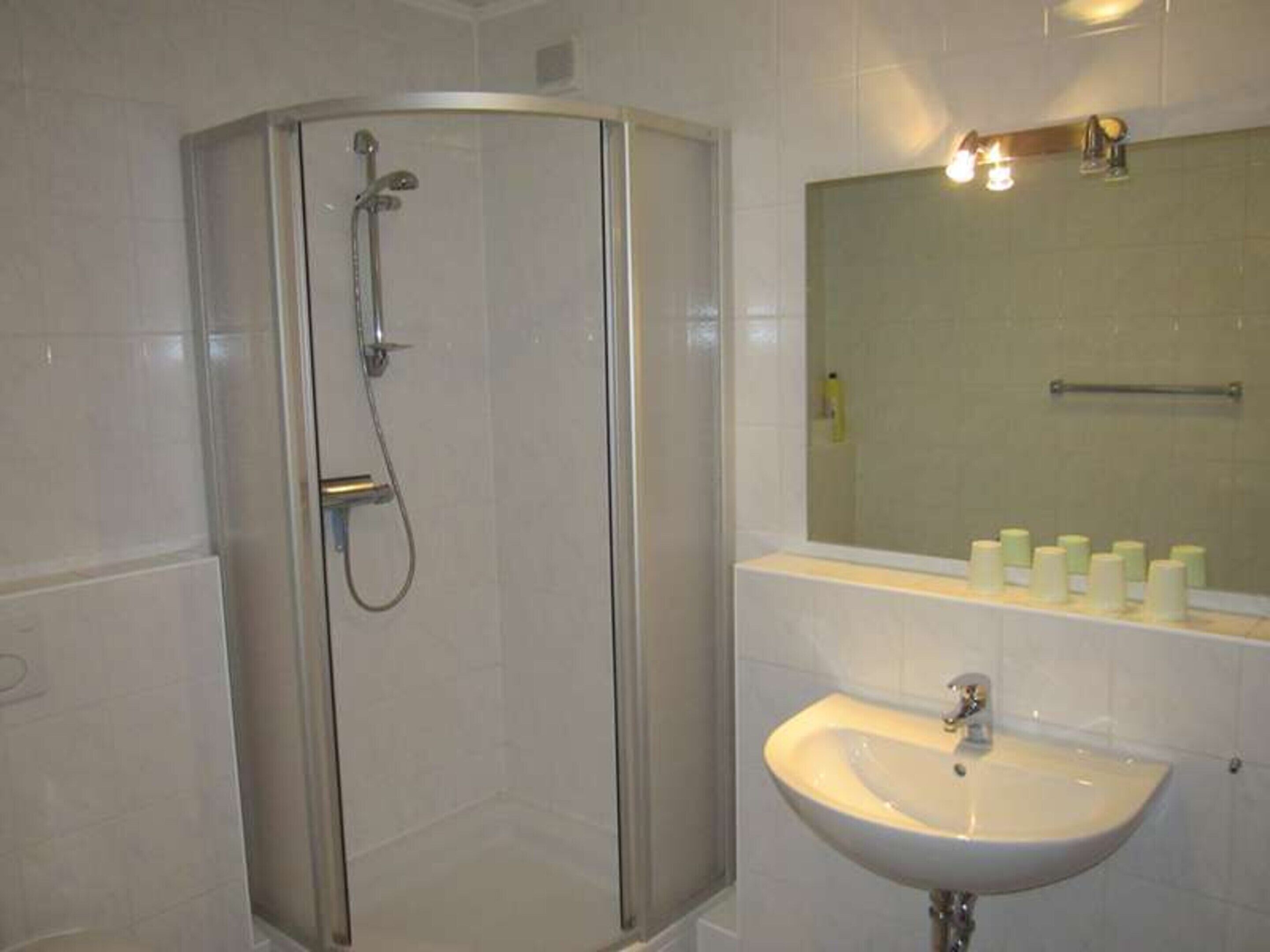 A bathroom with a glass-enclosed shower, a sink, and a mirror above it.