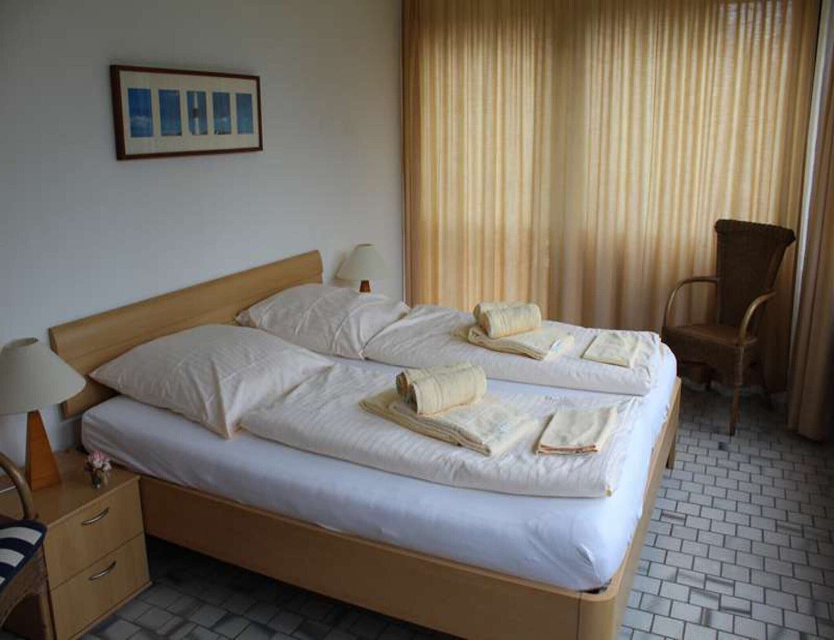 Habitación de hotel con cama doble, dos mesitas de noche, una silla y ventana con cortinas.