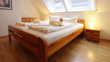 A wooden bed in a room with a sloped ceiling and skylight, a bedside table, and a nightstand.